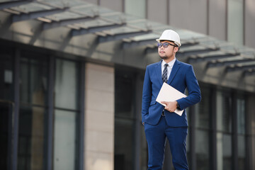 Young handsome asian engineer wearing in suit. holding tablet with white safety helmet looking...