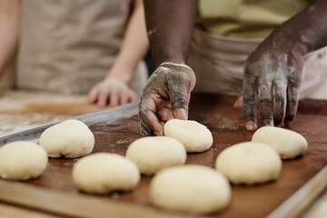 Fototapeta premium Close up of man carefully shaping dough for buns while working in artisan bakery, copy space