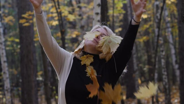 a beautiful blonde 40-49 years old walks in the autumn forest and throws up fallen maple leaves. slow motion. feelings and emotions, a walk in autumn
