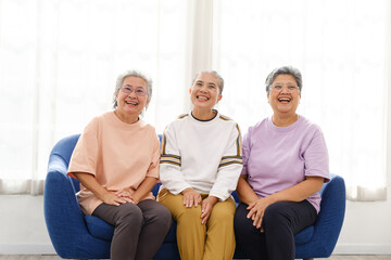 The group of happy and healthy three Asian senior women sits together on a sofa. Smiling and laughing together.