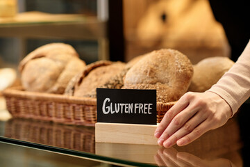 Closeup of fresh breads in artisan bakery with female hand holding gluten free sign, copy space