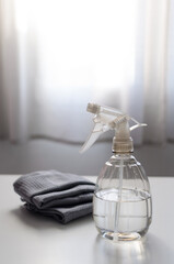 Spray bottle filled with pure water and vinegar and a cleaning cloth on a table against a bright window all in white and gray color. Environmentally friendly eco cleaning products concept. Zero waste.