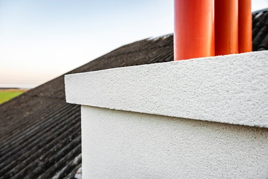 Applying white seamless concrete pebble-dash plaster on chimney.