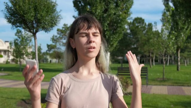 Teen suffer from hot unbearable summer. A modern young girl suffer from hot weather in the green summer park.