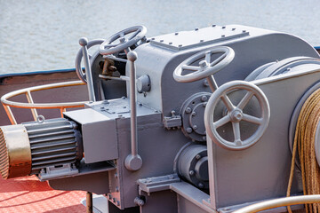 Closeup of levers, steering wheels, anchor windlass machine and heavy duty winches with tow rope at large mooring control station, bow of a cargo ship, blurred water in the background - obrazy, fototapety, plakaty