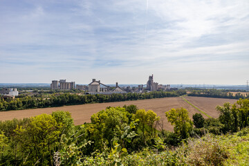 Agricultural field after harvest surrounded by green leafed trees next to cement factory,...
