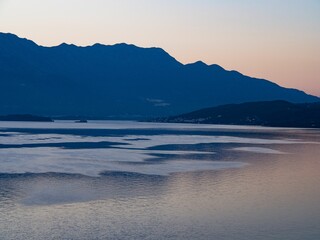 Obraz premium a blue lake at sunset with mountains in the distance and a boat out to sea