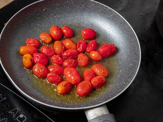 small red cherry tomatoes frying in olive oil in a pan