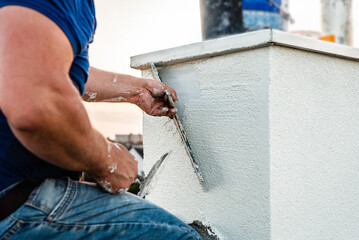 Worker applying white seamless concrete pebble-dash plaster on chimney using putty knife. © Natallia
