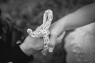 Close up picture of bride and groom's hands tied with white and green rope.