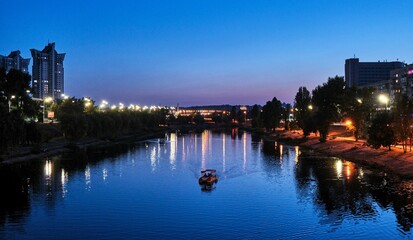 Naklejka premium Night skyline of the city of Kyiv, Ukraine with boats sailing along the Dnieper River