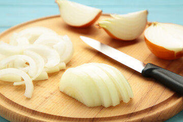 Whole and sliced yellow onions on wooden cutting board.