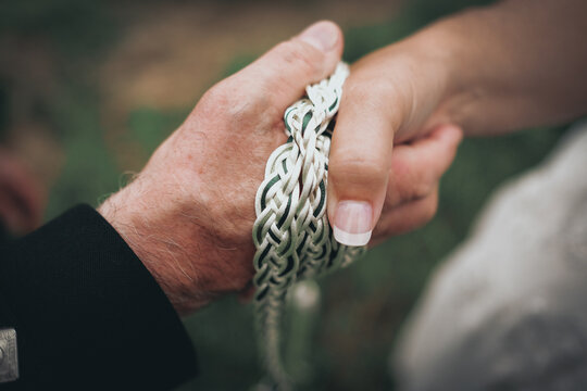 Close up picture of bride and groom's hands tied with white and green rope.