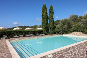 A swimming pool on the Montemassi hillside surrounded by cypresses and oleanders n the province of...