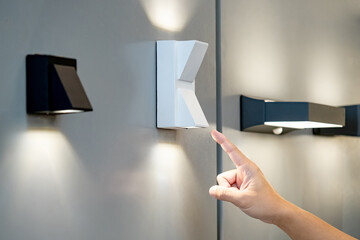 Designer hand pointing at sample of exterior LED wall lamp in home design store. Modern white...