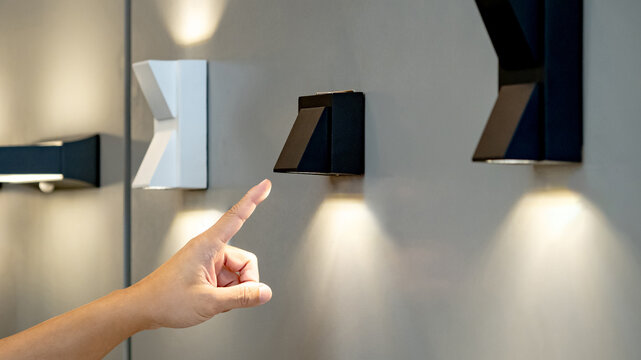 Designer hand pointing at sample of exterior LED wall lamp in home design store. Modern black downlight mounted on wall for outdoor lighting
