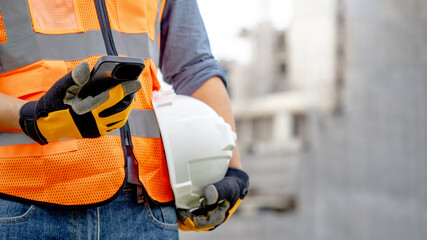 Construction worker man with orange reflective vest holding white protective safety helmet using...