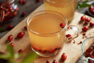 A cup of rose hip tea with fresh rosehips on a table
