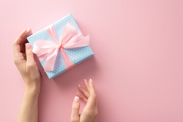 A heartfelt congratulations captured from first person top view: my hands gently touch a pastel blue gift box with polka dots, beautifully accentuated by a pink ribbon bow on a pastel pink canvas
