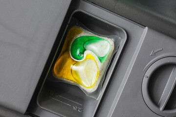 Dishwasher detergent dispenser. Closeup yellow and green washing pod. Cleaning capsules inside dispenser. Washing dishes background. Dishwasher part closeup. Pods cup part.
