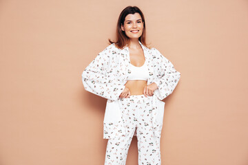 Obraz premium Young beautiful smiling female in trendy summer costume clothes. Carefree woman posing near beige wall in studio. Positive model having fun indoors. Cheerful and happy