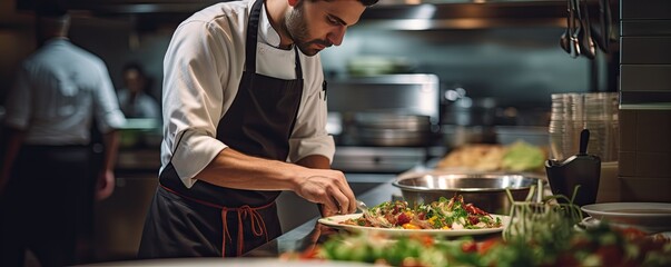 Cropped photo of a chef preparing a salad in a restaurant for visitors. Cook man neatly decorates the dish. Young professional chef adding some piquancy to meal. Format photo 5:2.
