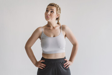 Young plus-size blonde woman in a crop top and sweatpants on a gray background with a surprised...