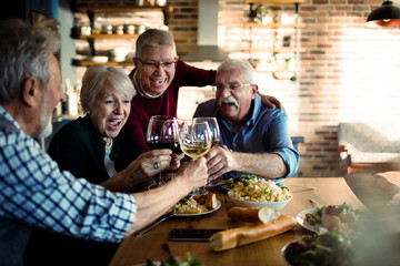 Senior friend group having wine and dinner at home together