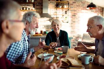 Group of senior friends having breakfast together in the kitchen - obrazy, fototapety, plakaty