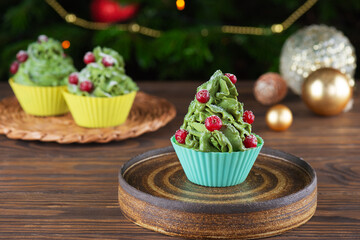 Green cupcakes with cranberries on a table on the background of the Christmas tree. Vegan, gluten, lactose, sugar free.