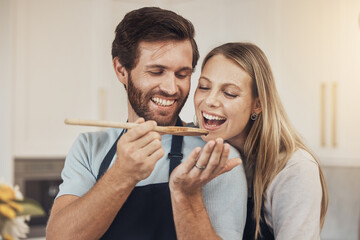Couple, cooking and taste test in kitchen with romance, support and love in their home together. Food, spoon and man feeding woman in house while preparing a delicious meal with fun and bonding - obrazy, fototapety, plakaty
