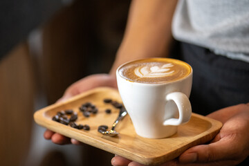 White ceramic cups of cappuccino with latte art Barista make coffee by pouring spills hot milk cream on black coffee. Barista serve holding cup of hot latte and coffee beans on wooden table cafe shop
