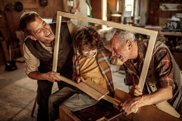 Fototapeta na wymiar Multigenerational family of male carpenters teaching their youngest one the ways in a carpentry shop