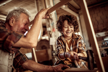 Senior male carpenter teaching his grandson how to use a hammer in a carpentry shop