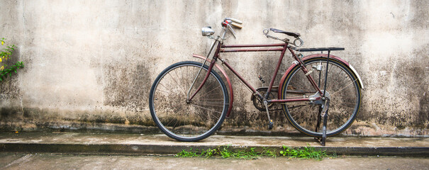 Banner panorama size of Vintage bicycle on old rustic dirty wall house, many stain on wood wall. Classic bike bicycle on decay brick wall retro style. Cement loft partition and window background.