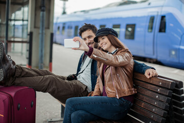 Young couple taking selfies on a smartphone while waiting for the train at the station