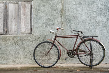 Foto op Canvas Vintage bicycle on old rustic dirty wall house, many stain on wood wall. Classic bike old bicycle on decay brick wall retro style. Cement loft partition and window background. © BESTIMAGE