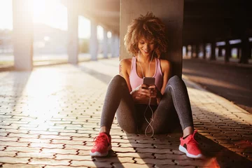 Tuinposter Young fit woman using a smartphone before jogging under a bridge in the city © Geber86