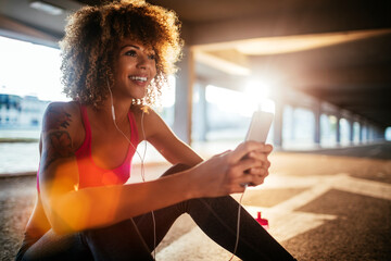 Young fit woman using a smartphone before jogging under a bridge in the city