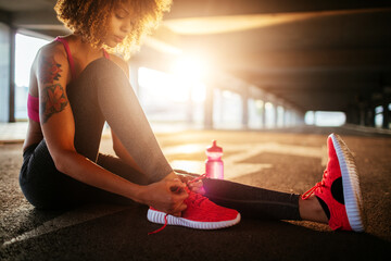 Young fit woman tying her shoelaces before jogging under a bridge in the city - obrazy, fototapety, plakaty