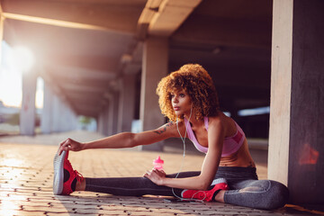 Young fit woman stretching before jogging under a bridge in the city
