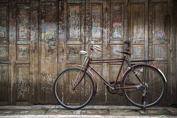 Vintage bicycle on old rustic dirty wall house, many text on wood wall. Classic bike old bicycle on decay brick wall retro style. Cement loft partition and window background.