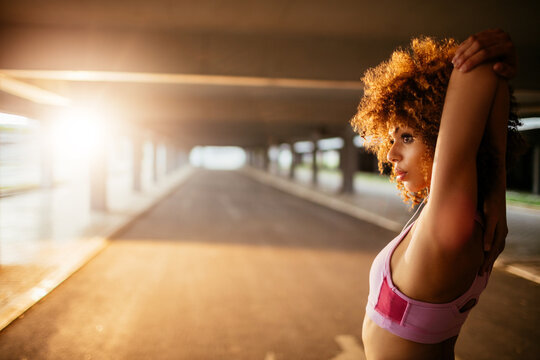 Young fit woman stretching before jogging under a bridge in the city