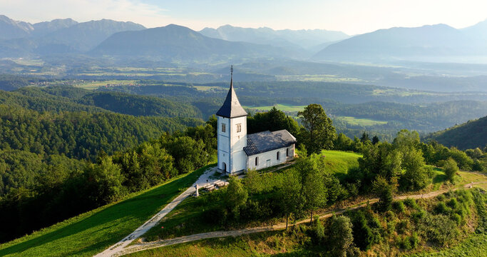 Aerial perspective, sunrise over St. Primoz Church in Jamnik on lush Slovenian hill, Kranj, Gorenjska
