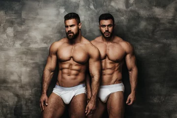 Poster Two naked men standing near textured wall. Two fitness male models in white underwear posing in studio. Couple of muscled hunks looking at camera. © Serge Lee