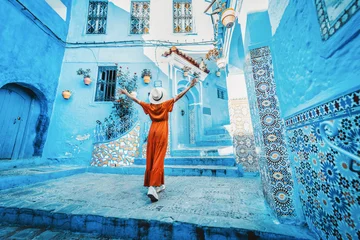 Zelfklevend Fotobehang Marokko Young woman with red dress visiting the blue city Chefchaouen, Marocco - Happy tourist walking in Moroccan city street - Travel and vacation lifestyle concept