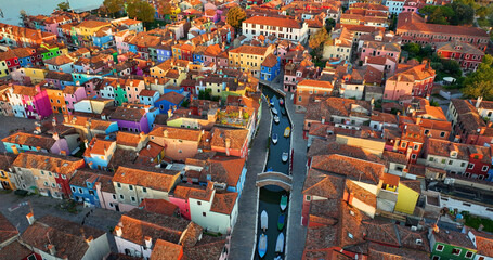 Aerial view of Burano colorful houses, along the Fondamenta embankment, featuring fishing boats and bridges, Venice, Italy at sunrise golden hour