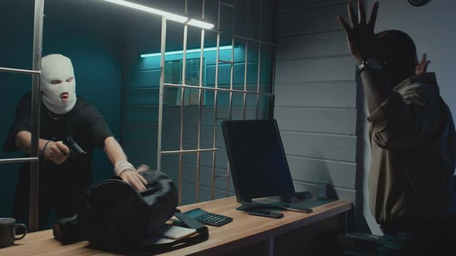 POV side shot of black male threatened pawnbroker putting money in black bag for young Caucasian robbers and hiding under the table in pawnshop