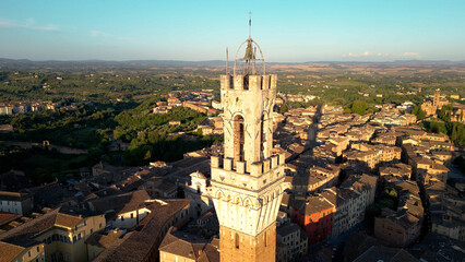 Siena, bell tower of the Torre del Mangia (Mangia Tower) and the surrounding old city of Siena, Tuscany, Italy. Aerial view at sunset