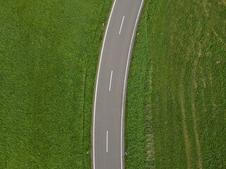 Curved road between green grass fields in the landscape 